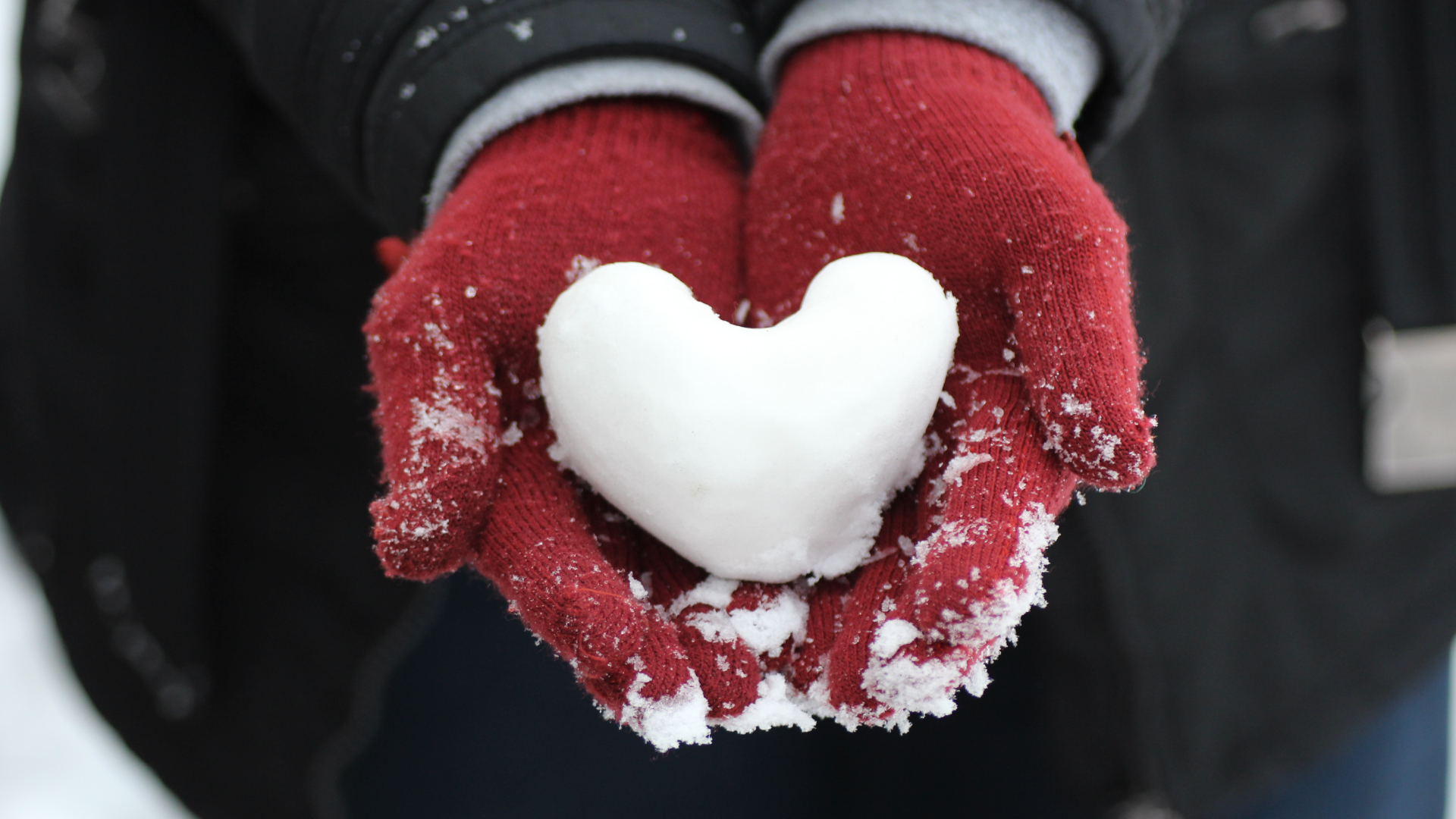 snow heart held by red gloved hands