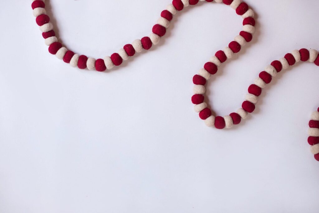 A white and red woolen beaded garland stretches across the top corners of the image against a white backgroumd.