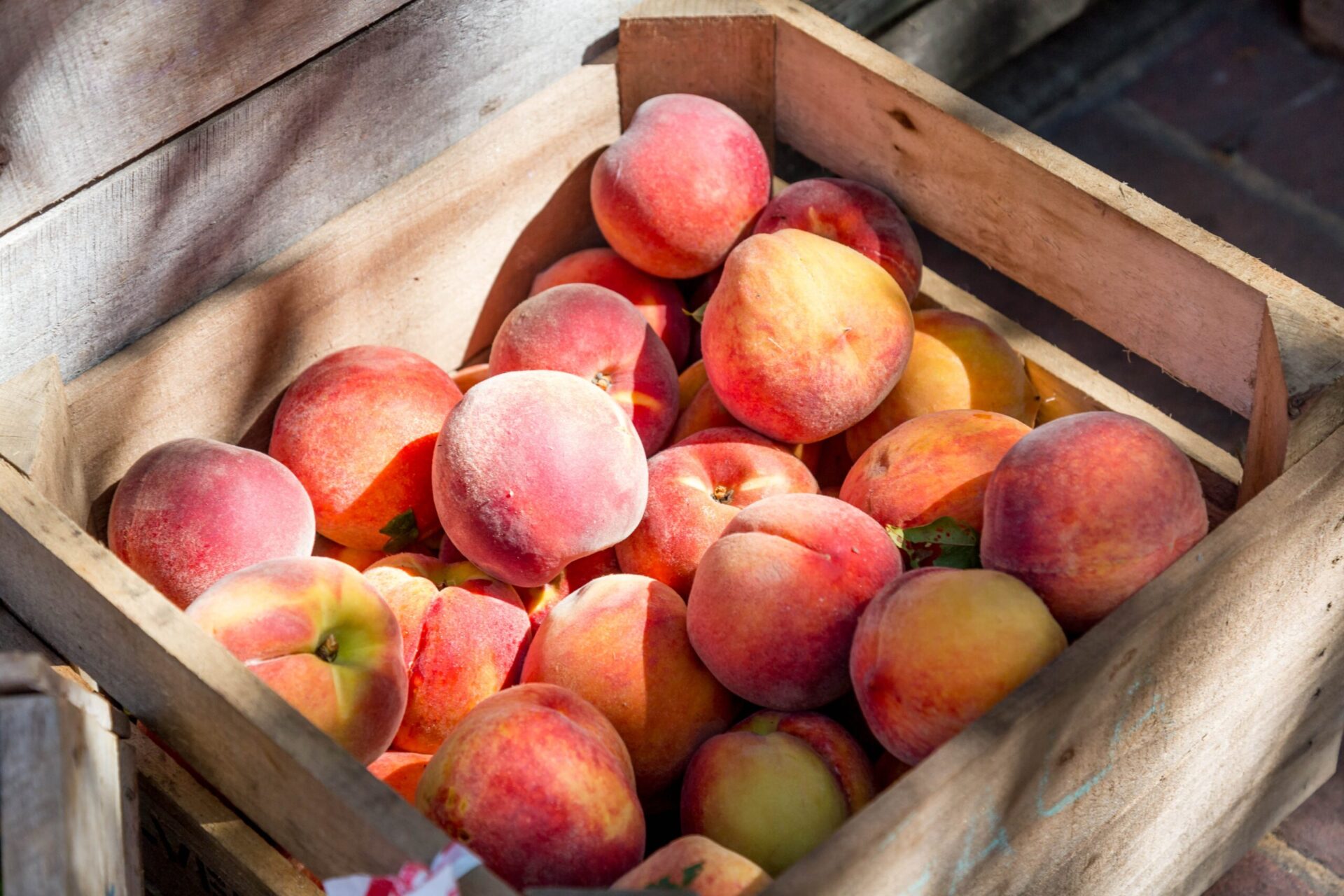 A wooden crate filled with peaches sit in dappled sunlight.