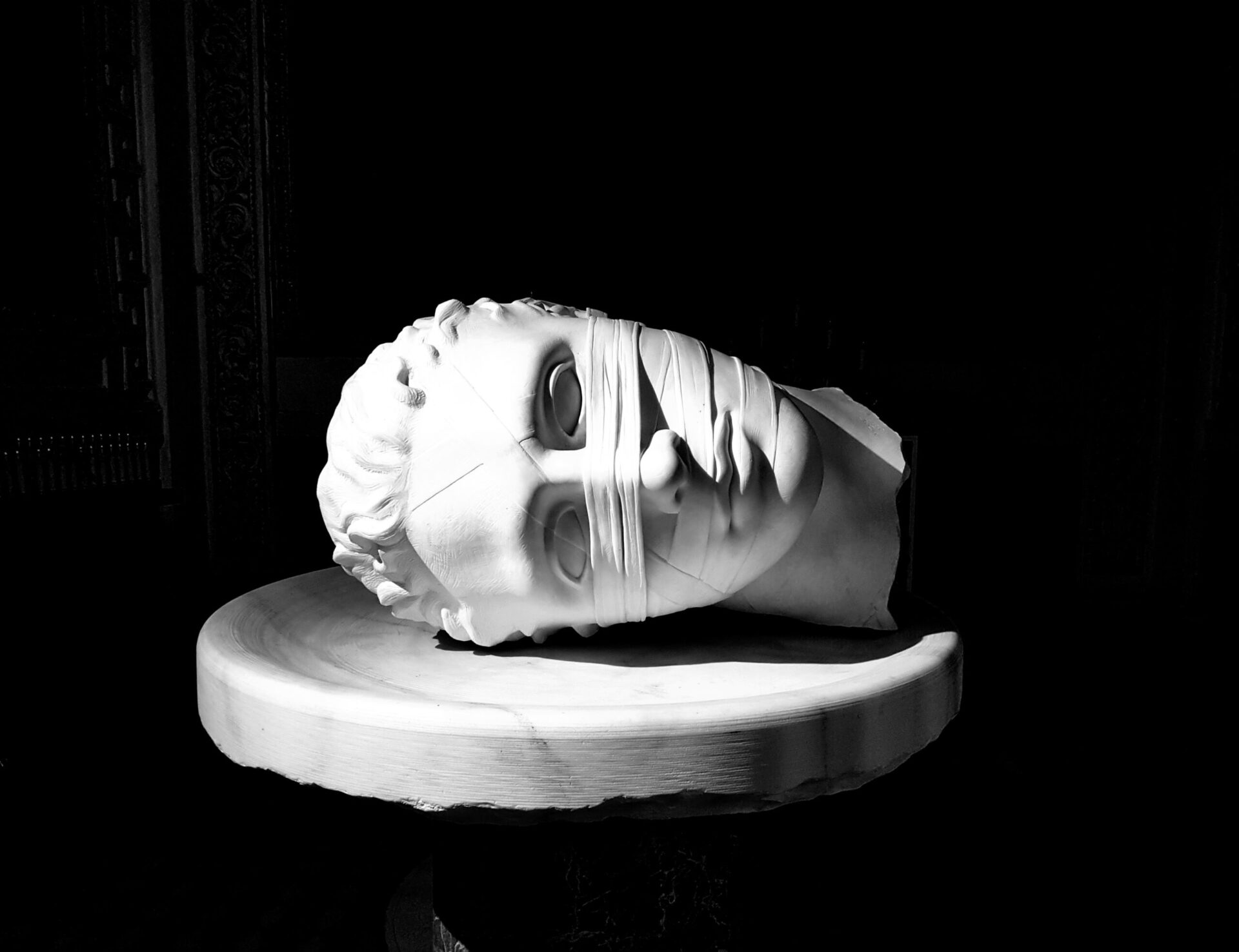 A white ceramic bust lays sideways on a white plinth against a black background.