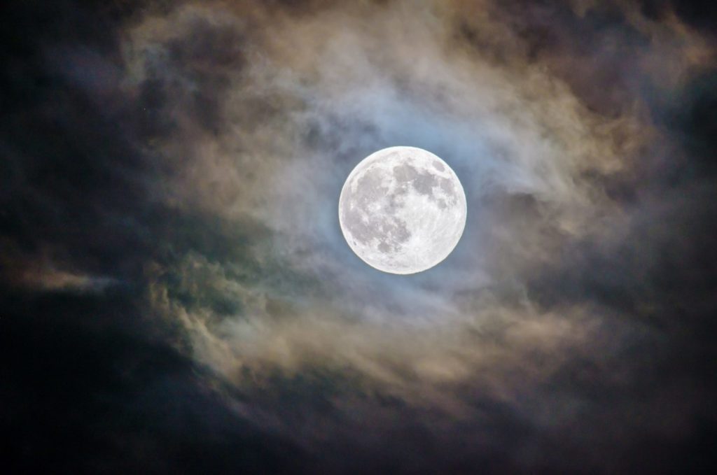 A large full moon hangs in a dark sky, surrounded by clouds.