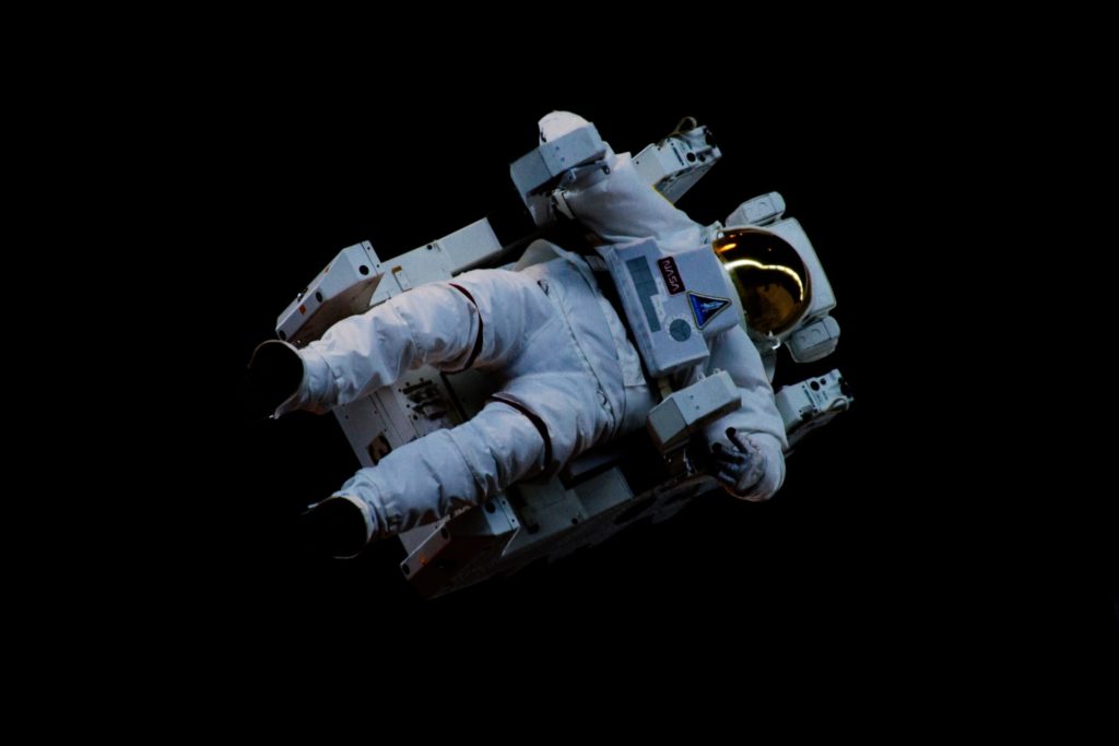 An astronaut in full space suit hangs in space, tilted at a 45 degree angle towards the right corner of the photo.