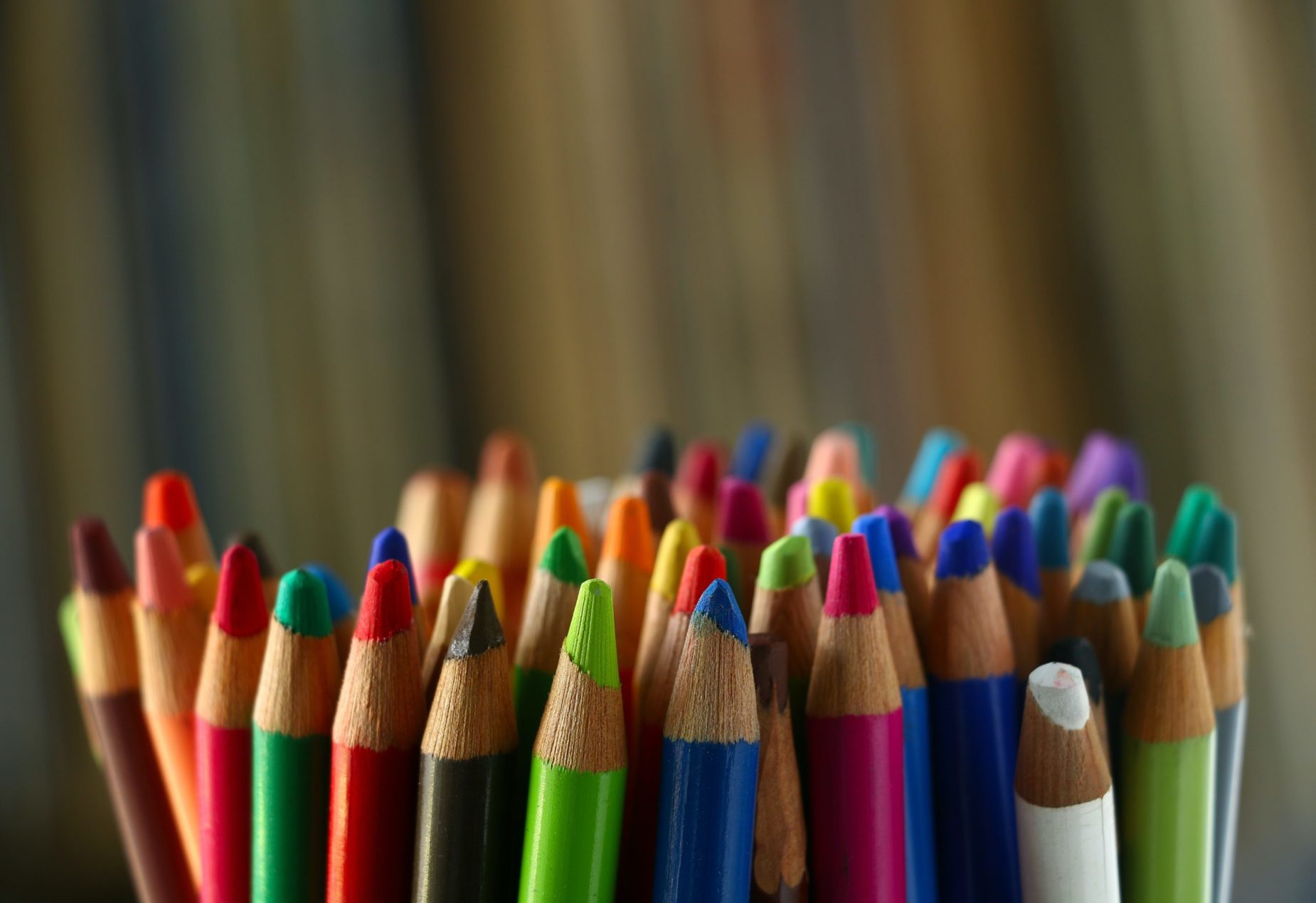 A large handful of colored pencils is in focus against a blurred, seemingly striped background.