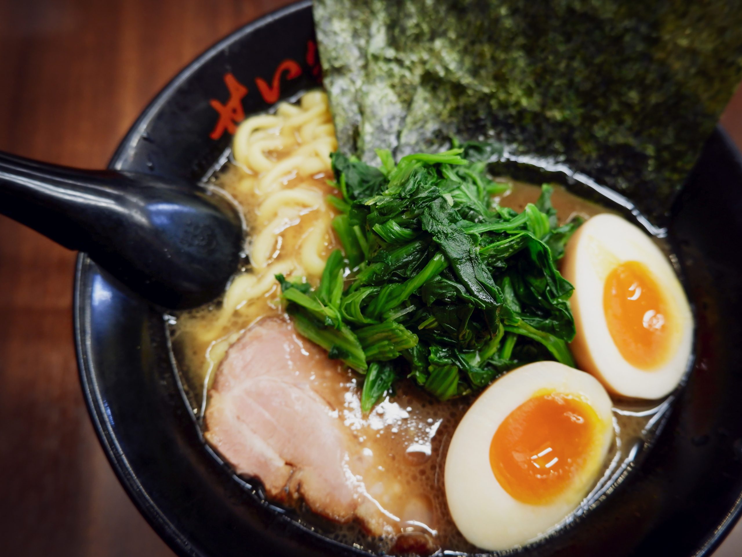 A bowl of ramen with noodles, meat, nori, greens, and a soft boiled egg.