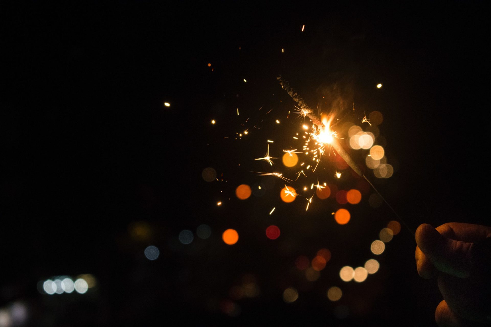 A sparkler is held by a hand against a black background.