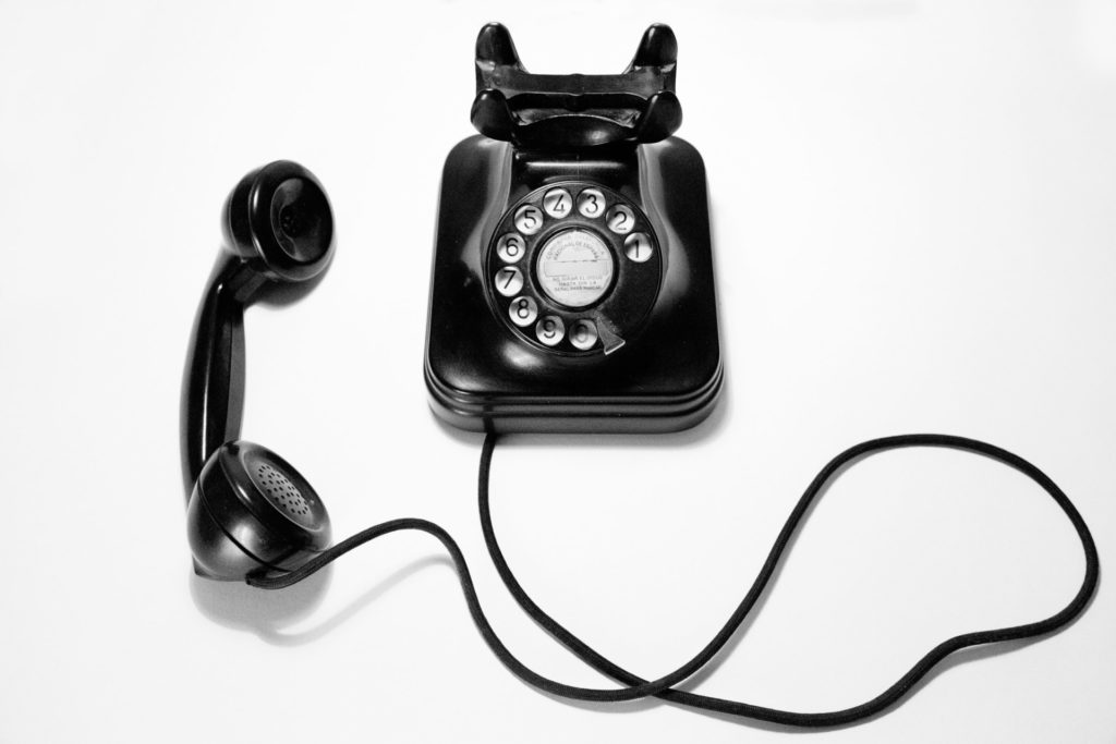 A black rotary style phone with a connecting cord rests on its side, off the receiver.